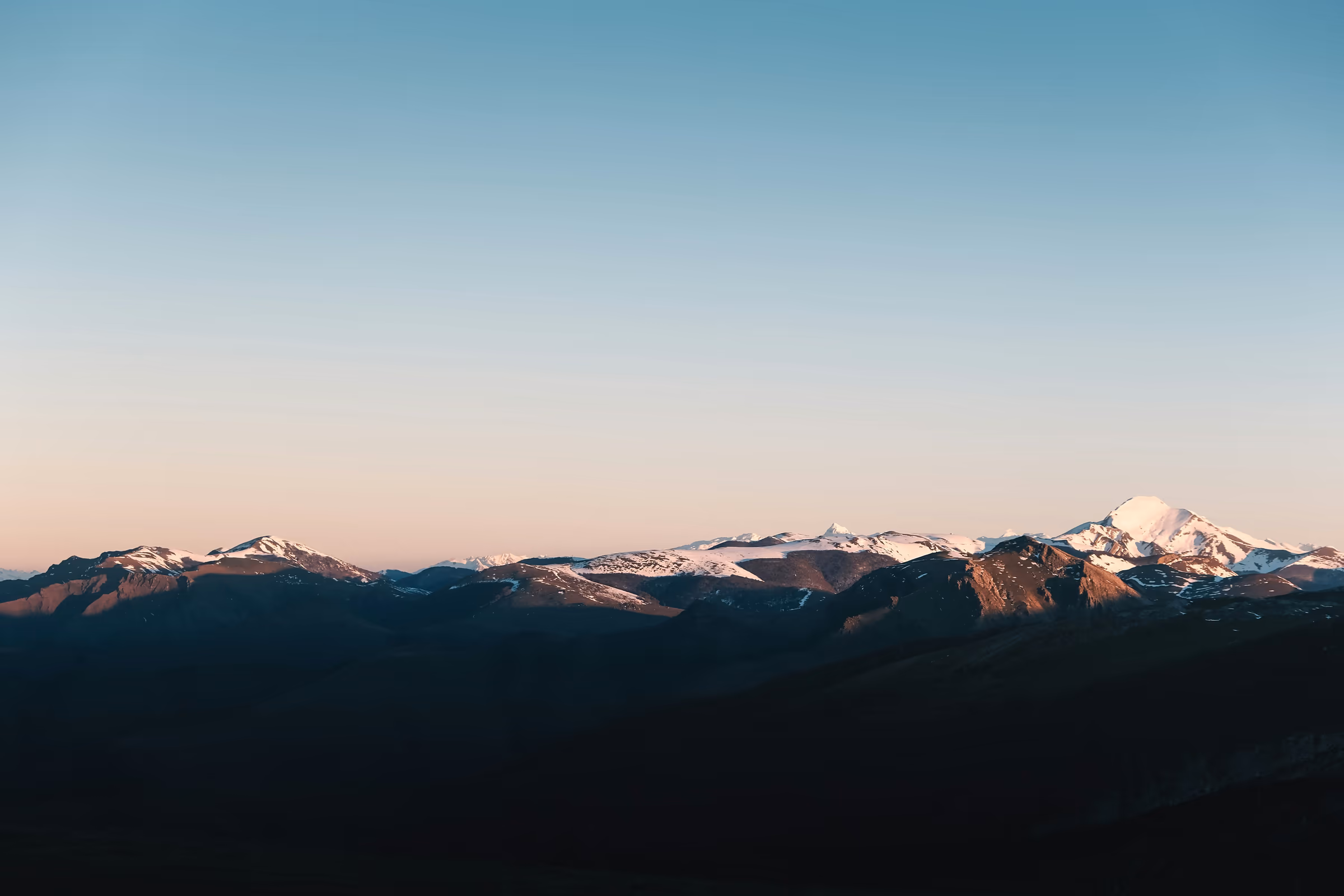 Snow-capped mountains under a clear sunrise sky